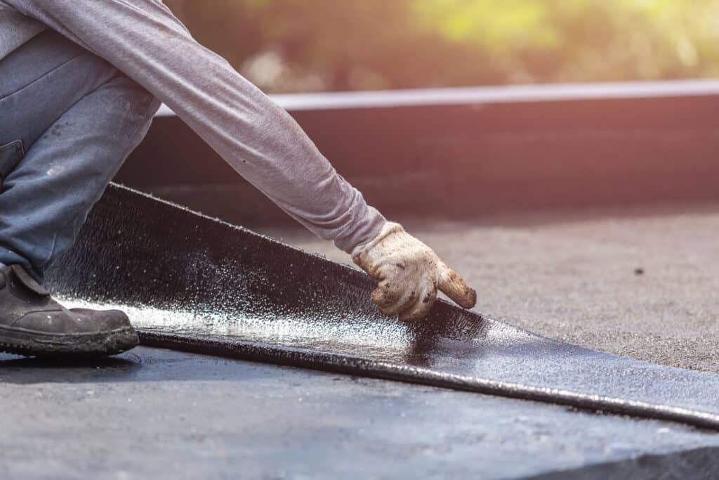 Groupe de travailleurs installant une feuille de goudron sur le toit du bâtiment