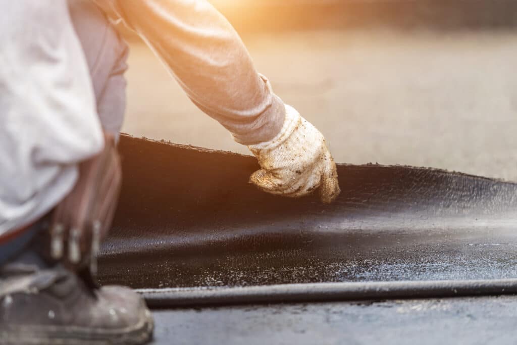 Groupe de travailleurs installant une feuille de goudron sur le toit du bâtiment